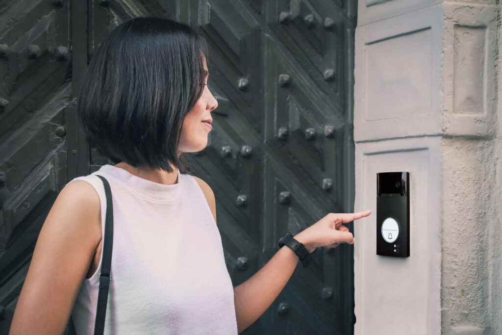 Girl that is pushing a button of the house intercom outdoors in front of a huge antique door.