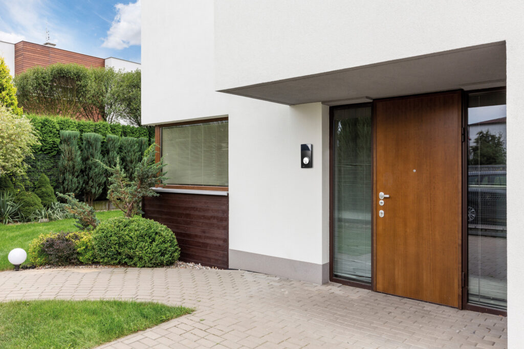 Wooden entrance door to modern white house with paving footpath and backside garden